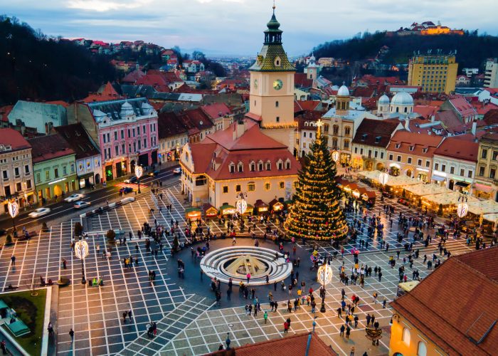 Aerial drone view of The Council Square at dusk in Brasov, Romania. Old city centre decorated for Christmas. County Museum of History, buildings, people